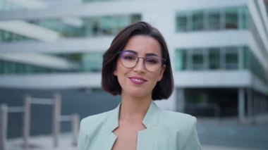 Smiling caucasian young woman in formal outfit looking to camera outside on street while feeling happy. Portrait of business modern manager showing sincere emotions