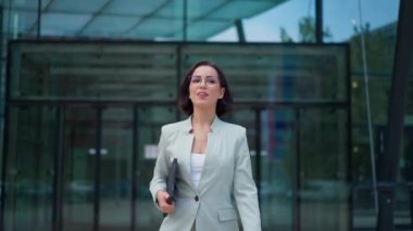 Successful young caucasian woman walking in central business district in modern city. Satisfied businesswoman carrying her laptop while going to the break after work