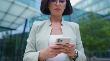 Close up successful businesswoman using phone at street. Serious business woman walking with phone outdoor. Female entrepreneur working with smartphone