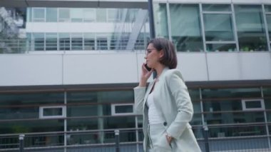 Successful female going to office in modern business center. Beautiful manager talking on a phone, having an Important business call outdoors