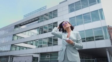 Low angle view of the confident businesswoman using smartphone while going through the street. Happy lady making work call in the urban space