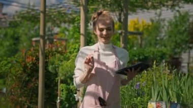 Portrait of caucasian happy woman florist browsing on tablet at floral store and dancing. Beautiful female entrepreneur of flower shop tapping on device at work. Floristry concept