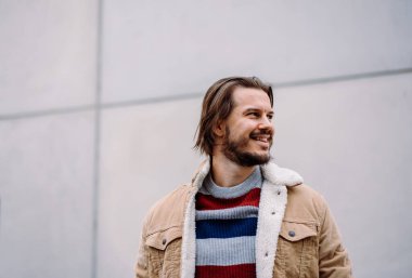 Gülümseyen erkek model boş duvarın üzerinde poz verirken mesafeye bakıyor. Ofis binasının yanında şık giyinmiş hippi bir adam işten sonra mola veriyor. Kentsel yaşam tarzı konsepti