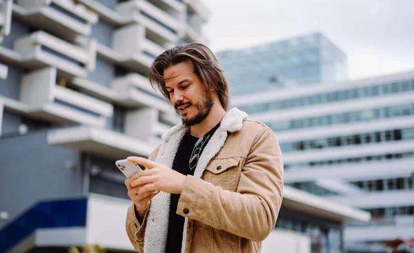 Neşeli stil sahibi adam şehirde yürürken mesaj yazıyor ve akıllı telefon ekranına bakıyor. Boş caddeden geçerken mobil cihazda uygulamayı izleyen beyaz adam