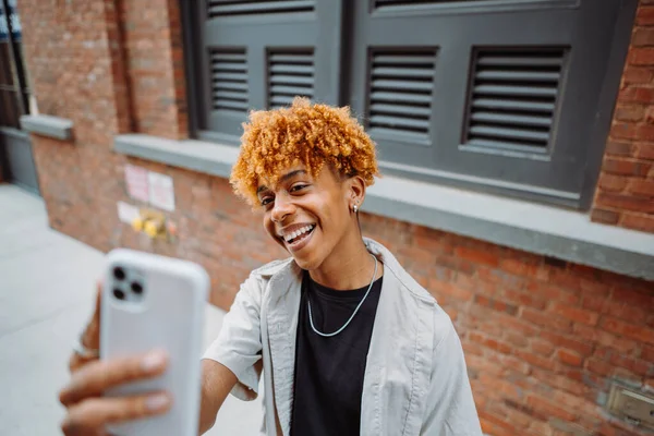 年轻的黑皮肤男子在街上摆姿势 并在城市背景下自拍 男人笑着在手机上拍照 幸福生活的概念 — 图库照片