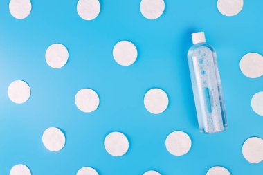 Pamuk pedler, toner şişesi ya da mavi arka planda su temizleme kabı, üst manzara. Güzellik, ten, saç veya vücut bakımı kavramı. Seçici odaklanma. Şeffaf plastik ambalajda sıvı güzellik ürünü