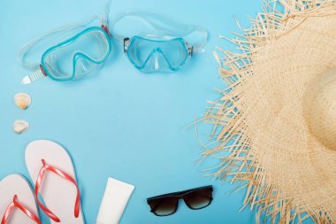 Güneş kremi dalış maskesi, spor ayakkabı, çalar saat, deniz kabukları, kamera, yukarıdan izole edilmiş mavi arka plan ve telif alanı. Düz yatıyordu