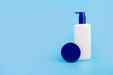 Doğal kozmetik krem beyaz şişe ve mavi krem kavanozu. Telif alanı olan izole edilmiş mavi arka planda cilt bakımı. Modelleme. Düzlük güzellik ve kaplıca konsepti