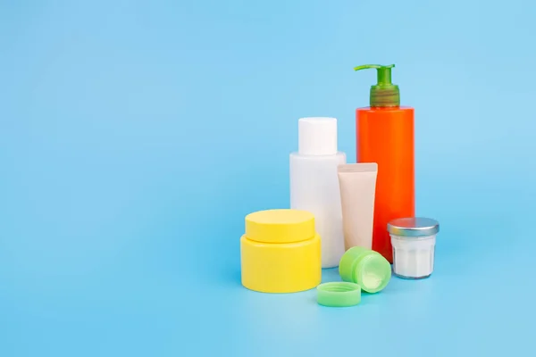 Doğal güzellik dermatolojisi kozmetik krem beyaz şişe ve turuncu şişe, sarı krema kavanozu, izole edilmiş mavi arka planda cilt bakımı. Modelleme. Düzlük güzellik ve kaplıca konsepti