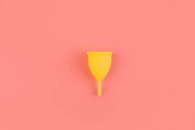 Silikon sarısı adet bardağı. Pembe arka plan yatağında kadın sağlığı ve alternatif hijyen. Çevre dostu, kadın hijyeni için alternatif yeniden kullanılabilir ürün. Minimalizm arka planı, monokrom.