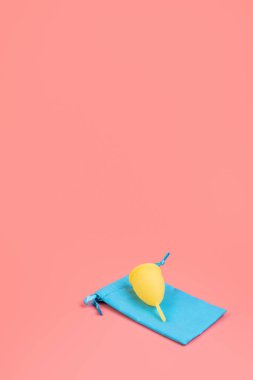 Mavi keseli silikon sarı aybaşı bardağı. Pembe arka planda kadın sağlığı ve alternatif hijyen. Çevre dostu, kadın hijyeni için alternatif yeniden kullanılabilir ürün. Dikey minimalizm.