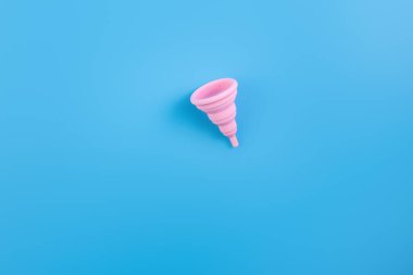 Silikon pembe regl kupası. Mavi arka planda yatan kadın sağlığı ve alternatif hijyen. Çevre dostu, kadın hijyeni için alternatif yeniden kullanılabilir ürün. Minimalizm arka planı