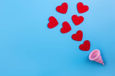 Silikon pembe regl fincanı düz. Kadın sağlığı ve alternatif hijyen. İçinde kan damlaları ya da mavi arka planda kırmızı kalpler olan bir fincan. Çevre dostu, kadın hijyeni için alternatif yeniden kullanılabilir ürün..