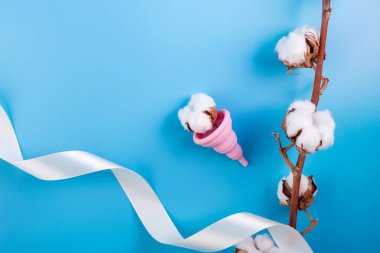 Pamuklu ve pamuklu silikon pembe adet kupası. Mavi arka planda kadın sağlığı ve alternatif hijyen. Çevre dostu. Minimalizm tek renk yumuşaklığı. Hijyen için alternatif yeniden kullanılabilir ürün.