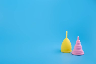 Silikon pembe ve sarı aybaşı bardakları. Mavi arka planda kadın sağlığı ve alternatif hijyen. Çevre dostu, kadın hijyeni için alternatif yeniden kullanılabilir ürün. Minimalizm yumuşak, organik.
