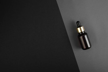 Gri, siyah geometrik arkaplan manzaralı, kahverengi pipetli cam bir şişe. Cilt ve saç bakımı için Aromatik Kozmetik Ürünler Organik doğal yağla güzellik ürünlerini nemlendirir