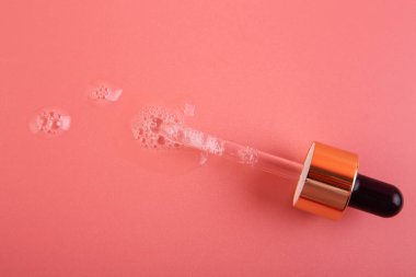 Açık pembe arka planda cam pipeti olan temiz bir serum döküldü. Sıvı kozmetik şeffaf ürün ve küçük hava kabarcıkları. Düz Yatay.