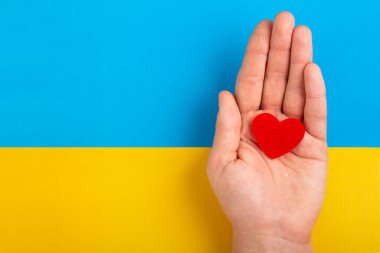 Genç bir Ukraynalı kadının eli sarı-mavi arka planda kırmızı bir kalp taşıyor. Ukrayna halkının Rusya 'yla savaşa katılma kavramı. Savaş konsepti değil