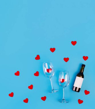 Top view photo of romantic evening, dinner decor hearts love wineglasses with confetti wine bottle on isolated blue background with copyspace