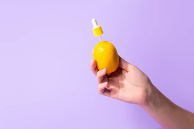 Metaphor, bottle serum with vitamin C for skin in lemon in female hand. The concept vegetable cosmetics and aromatherapy.
