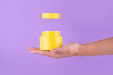 Jar of moisturizing facial cream. Yellow plastic container with cream vitamin c on purple background. Yellow unbranded, balsam, face or hand creme jar mockup