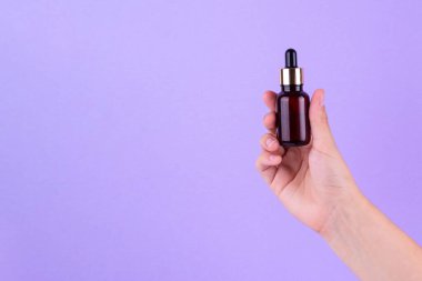 Serum bottle in female hands, top view. Transparent moisturizer for skin care. Nourishing essential oil in glass bottle with pipette. Liquid emulsion with hyaluronic acid. Beauty cosmetic spa product