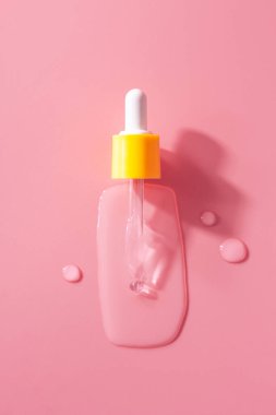 Yellow pipette drops of serum moisturized bottle on pink background. Essence transparent hyaluronic acid close up. Spa, beauty, skincare product.