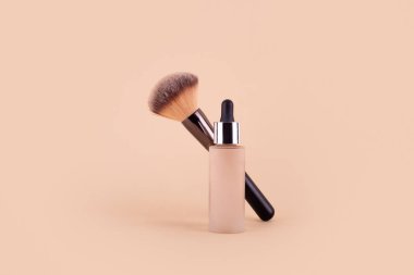 Liquid foundation cream unbranded bottle with makeup brush. Facial correction, liquid concealer, tone, bb, cc cream skincare product on beige background. Feminine cosmetics accessory with copy space