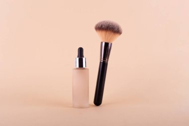 Liquid foundation cream unbranded bottle with makeup brush. Facial correction, liquid concealer, tone, bb, cc cream skincare product on beige background. Feminine cosmetics accessory with copy space