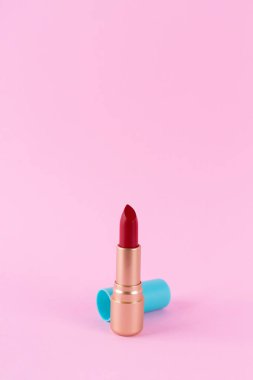 Red lipstick in a golden tube isolated on a pink background. Cosmetic product for bright beauty creative makeup. Make-up artist tool