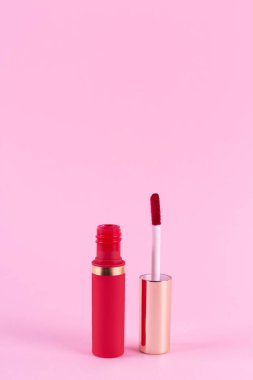 Lipstick and applicator wand on pastel pink background. Liquid lip stick red lip gloss open tube. Makeup cosmetic product. Top view, flat lay, copy space