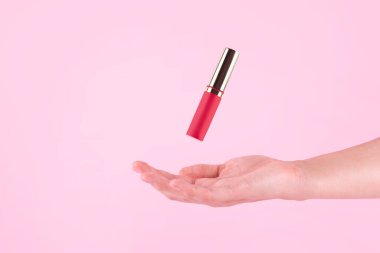 Female hand holding red lipstick. Equipment for maquillage. Make-up and visagist. Place for text or creative design. Mockup style. Cosmetic and beauty concept. Isolated on pink background