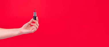 Tool for maquillage. Female hand holding lipstick. Make-up and visagist. Cosmetic products and beauty concept. Isolated on red. Mockup style, place for text or creative desig