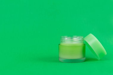Opened green jar with cream on isolated green background close up. Brand packaging mockup. Aromatic oil, skincare beauty product, cream or serum. Natural herbal cosmetics concept
