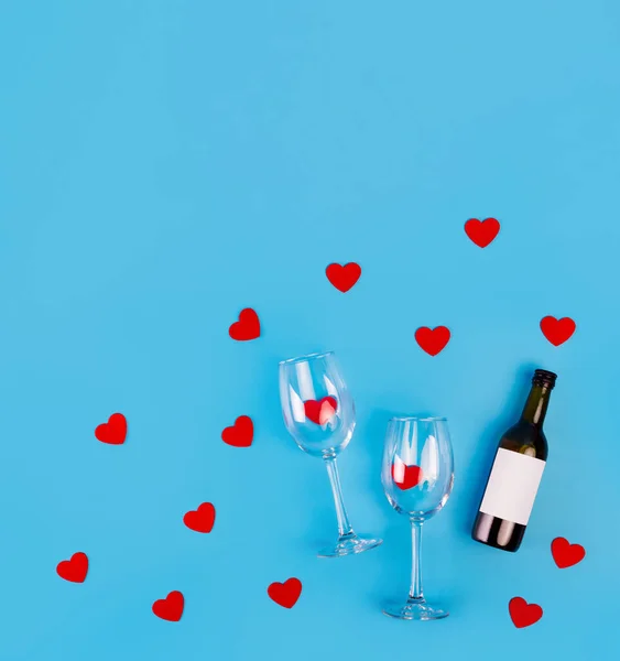 Top view photo of romantic evening, dinner decor hearts love wineglasses with confetti wine bottle on isolated blue background with copyspace