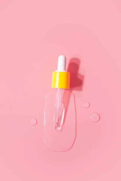 Yellow pipette drops of serum moisturized bottle on pink background. Essence transparent hyaluronic acid
