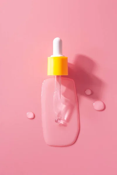 Yellow pipette drops of serum moisturized bottle on pink background. Essence transparent hyaluronic acid close up. Spa, beauty, skincare product.