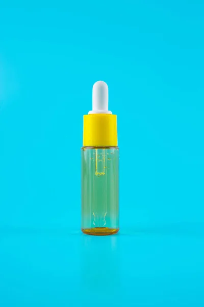glass yellow bottle with pipette with essential oil on a blue background top view. Aromatic cosmetic product for skin hair care Moisturizing beauty product with vitamin C close up