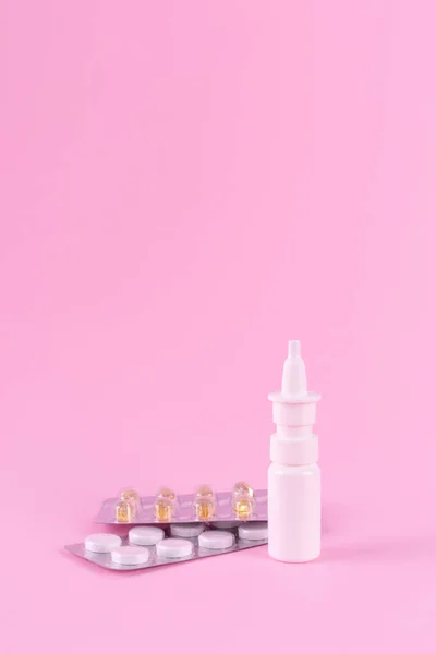 Medicines for the treatment of colds and viral diseases. White tablets, capsules, throat lozenges and nasal spray isolated on a pink background