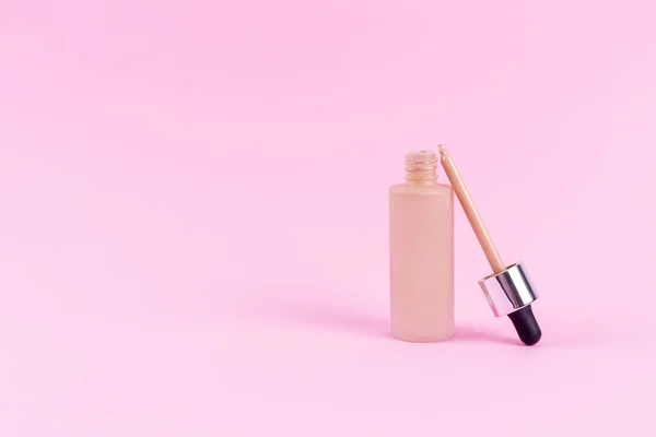 Opened liquid foundation cream with pipette unbranded bottle on a pink background. BB cream for professional make-up, eyedropper for applying to the face. Cosmetic female accessory, fluid. Mock up