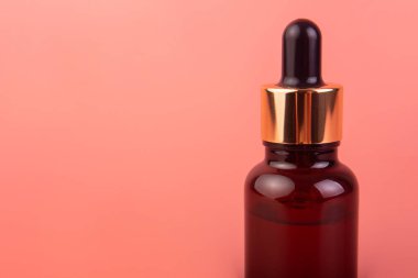 Brown bottle with dropper with a beauty serum on pink background. Glass packaging for cosmetic product, essential aroma oil. Skin care, hydration and nutrition with collagen.