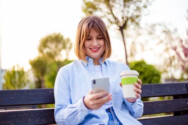 Photo of charming pretty young lady communicating modern gadget sitting bench smiling outside urban city street