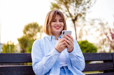 Photo of charming pretty young lady communicating modern gadget sitting bench smiling outside urban city street
