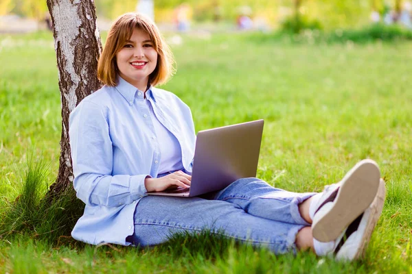 Photo portrait of pretty young woman smiling teeth sitting in green park working on laptop smiling