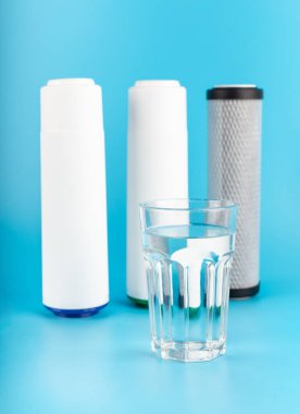set three of cartridges for water filter with clear glass of water isolated on blue background. Concept of water treatment technology. filter cartridges to domestic water treatment system