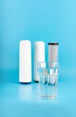 set three of cartridges for water filter with clear glass of water isolated on blue background.  Concept of water treatment technology. filter cartridges to domestic water treatment systems 