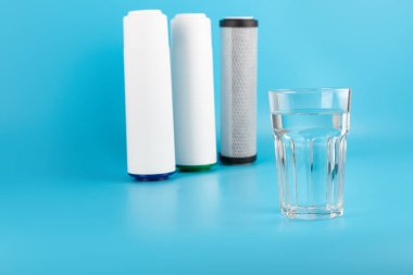 set three of cartridges for water filter with clear glass of water isolated on blue background.  Concept of water treatment technology. filter cartridges to domestic water treatment systems 