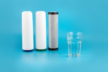 set three of cartridges for water filter with clear glass of water isolated on blue background.  Concept of water treatment technology. filter cartridges to domestic water treatment systems 