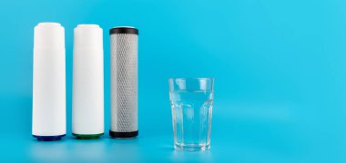 set three of cartridges for water filter with clear glass of water isolated on blue background.  Concept of water treatment technology. filter cartridges to domestic water treatment systems 