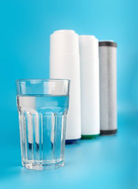 set three of cartridges for water filter with clear glass of water isolated on blue background.  Concept of water treatment technology. filter cartridges to domestic water treatment systems 